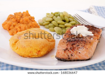 Sweet Potato Biscuit on white plate with baked Salmon Steak, lima beans and candied yams.  Strong light on white background.