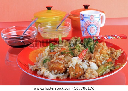 General Tso Chicken Chinese Dinner on red plate with red chopsticks against red background with reflection in glass top table.