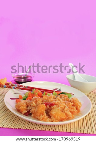Sweet and Sour Chicken Dinner in Chinese Restaurant setting on bamboo cane place mat and design on plate.  Colorful background with copy space -- vertical format