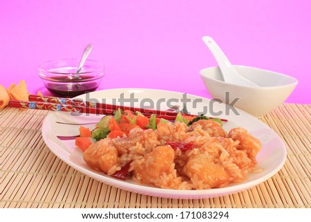 Sweet and Sour Chicken Dinner in Chinese Restaurant setting on bamboo cane place mat and design on plate.  Colorful background with copy space.