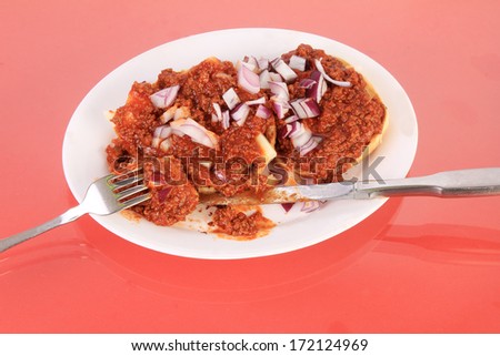 Taking a bite of Sloppy Joe mix spread over sesame bun with mozzarella cheese and sprinkled with chopped red onion.  Served on white plate reflecting in red glass-top table.