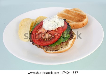Dollop of sour cream and dill on turkey burger sandwich with sliced tomato and lettuce.