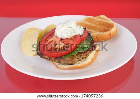 Dollop of sour cream seasoned with dill on turkey burger sandwich.  Snack for health conscious diners.  White plate with reflections on glass top table.