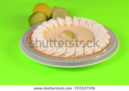 Key Lime Pie in aluminum pie pan on lime green background with slice of lime in center.