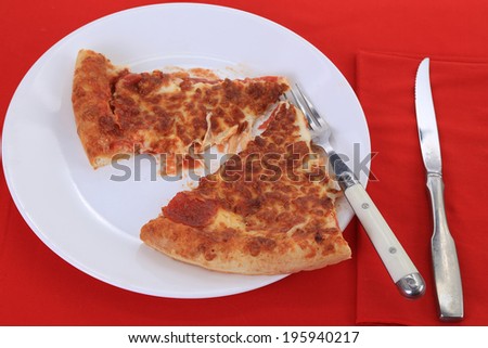 Slices of pepperoni pizza with extra cheese on white plate and red background.