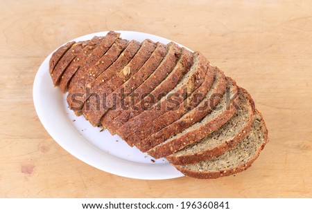 Fresh baked loaf of pumpkin seed bread on white plate on wooden cutting board.  Multiple grains and whole wheat flour with slight sweetness from addition of molasses.