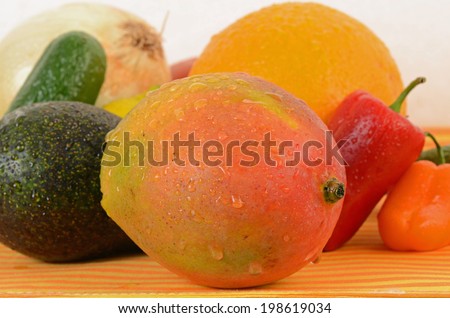 Fruit and vegetable Ingredients for making Spicy Mango Salsa spread over orange and yellow striped base with neutral background.