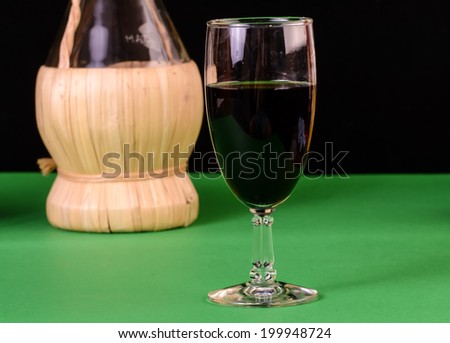 Stemmed glass of dark red Chianti Wine in foreground with straw-wrapped wine bottle in background.