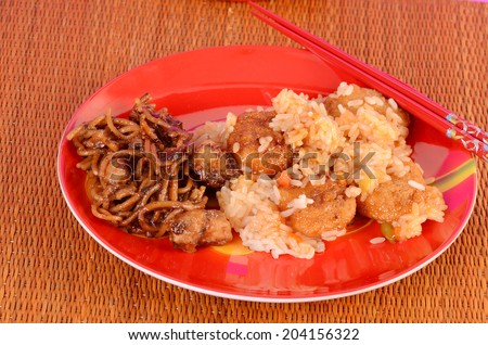 Sweet and Sour Chicken on red plate sitting on bamboo mat with chopstick and side dish of General Tso\'s Chicken with noodles.