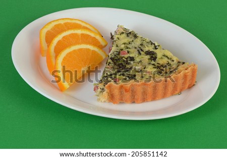 Near perfect crust of Spinach Quiche with ham and cheese is focal point of this appealing brunch plate with orange slices on green background.