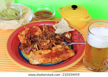 Enchiladas on colorful plate with rice and beans.  Avocado and chips and mug of frothy beer.