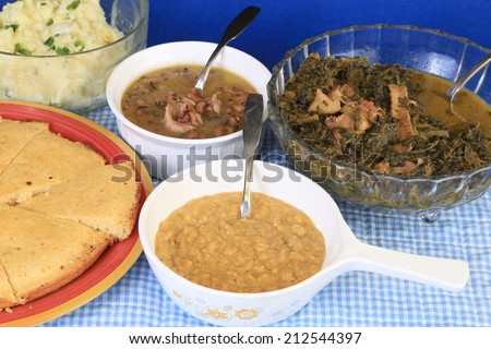 Soul Food Supper served family-style on blue gingham background -- creamed corn; black-eyed peas; collard greens; mashed potatoes and corn bread.