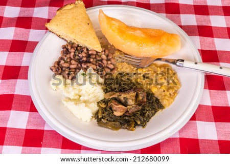 Collard greens in bacon fat; creamed corn; mashed potatoes; black-eyed peas; cantaloupe and corn bread on traditional red plaid tablecloth.