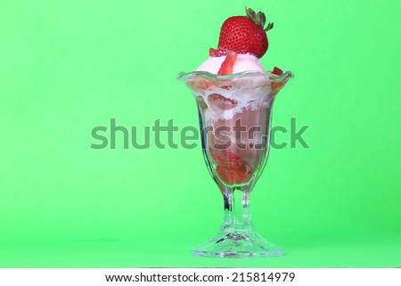 Combination of chocolate and vanilla ice cream with chopped strawberries in vintage tulip sundae glass on green background.  Topped with fresh ripe strawberry.