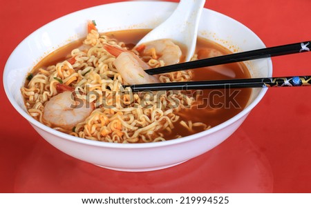 Bowl of Chinese Noodle Soup with shrimp on red background with black chopsticks and Asian Soup Spoon.