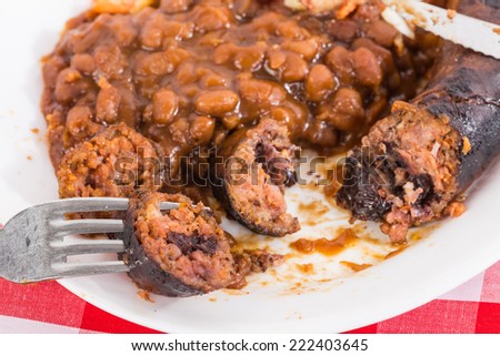 Grilled Jalapeno and Black Cherry Sausage on white plate with sweet baked beans.