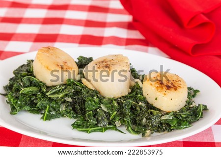 Large Sea Scallops fried crispy on top  on bed of steamed kale -- simulating Sea Weed. Against bright red setting.
