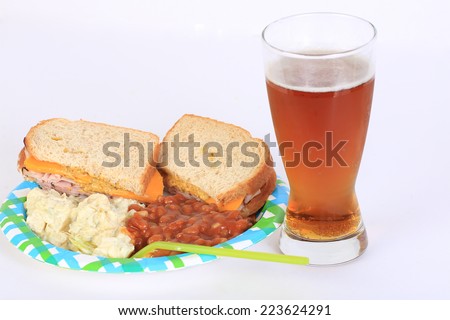 Ham and Cheese on honey wheat bread on paper plate with potato salad and baked beans with glass of beer.