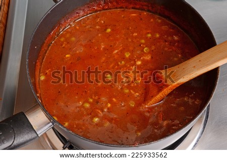 Boiling hot homemade vegetable soup in medium sauce pan on electric stove with wooden stir spoon.