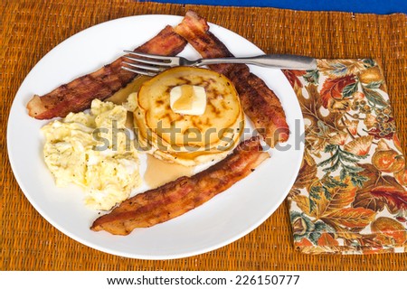 Large breakfast of scrambled eggs, bacon and stack of buttered pancakes.