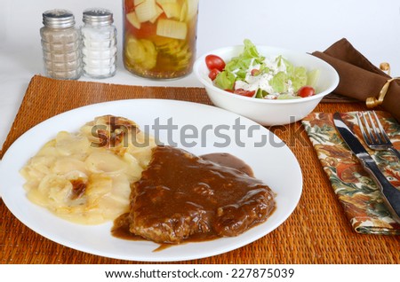 Typical Country Cooking Dinner of Chicken Fried  Steak in brown gravy with Scalloped Potatoes.  Fruit jar of pickled vegetables in background.  Set in Autumn Colors.