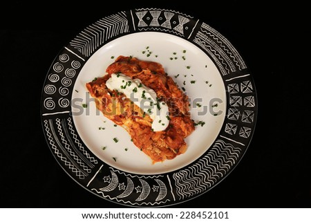 High contrast image of Chicken Enchiladas on black and white plate with Aztec Graphics isolated on black background with copy space.