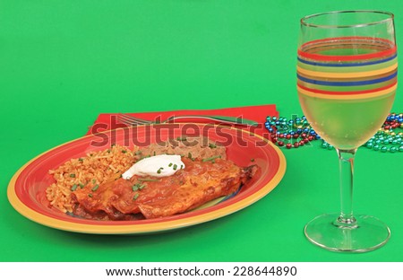 Dollop of sour cream atop red chicken enchiladas with rice and beans in brightly colored plate against green background.