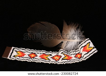 Colorful beaded bracelet in Native American pattern with feather against black background.