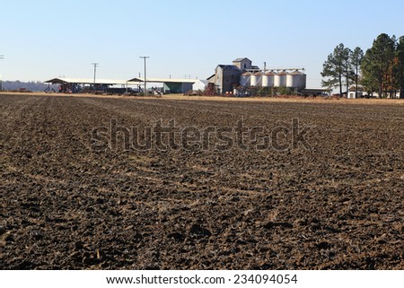 Large black land farm in Eastern Arkansas with plowed field laying fallow.  Seed and grain silos in background with sheds and farm equipment.