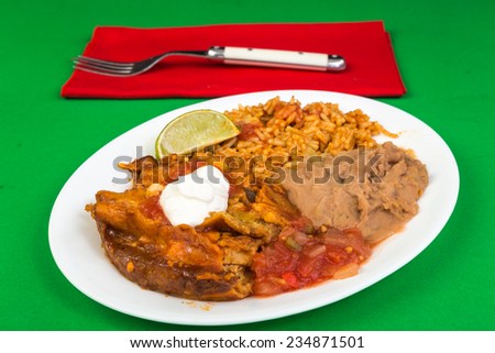 Mexican dinner - chicken enchiladas on white plate with rice and beans in red, green and white colors of Mexican Flag.