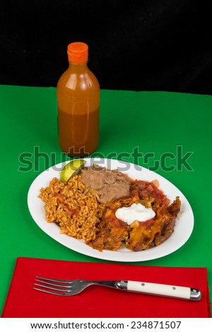 Chicken enchiladas on white plate with beans and rice against green background.  Red white green colors of Mexican Flag.
