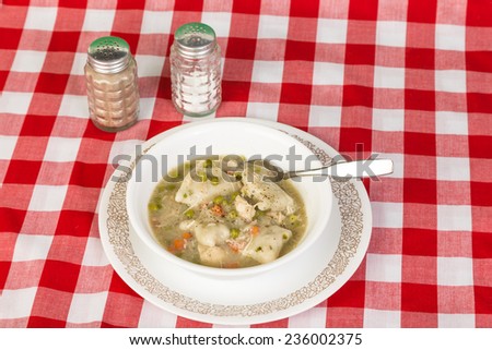 Southern soul food cooking - chicken and dumplings in bowl on red plaid tablecloth country kitchen setting.