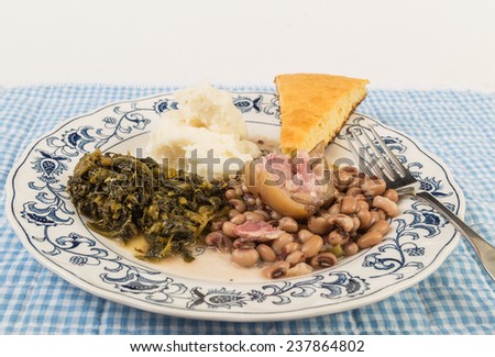 Large piece of fat ham hock in black-eyed peas with collard greens and mashed potatoes and slab of cornbread.