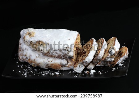 Cranberry Stollen on black cake plate against black background.  Sugar-coated loaf with slices ready to serve.