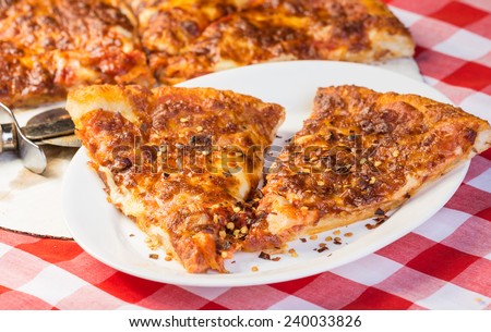 Two slices of pepperoni pizza with extra cheese on white plate with takeout pizza in background with pizza knife.