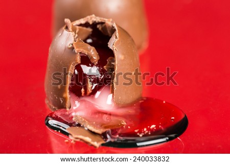 Two pieces of chocolate covered cherry candy on red background with one broken and syrup spilling out on red background with copy space.