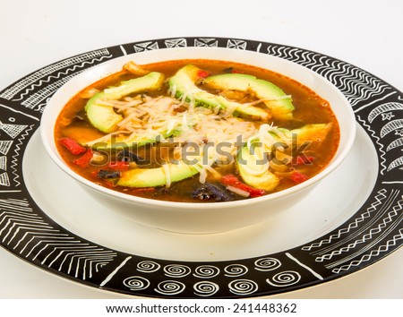 Tight shot of bowl of tortilla soup in white bowl on graphic black and white charger plate.  Ancient Aztec Geometric Pattern on plate.