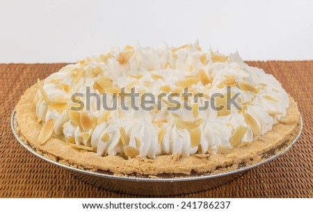 Whole Banana Cream Pie in aluminum pie pan on wicker place mat.   Garnished with sliced almonds