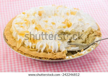 Strong back light and selective focus on Banana Cream Pie on Pink Gingham tablecloth.  Pie Knife with piece cutout.  Country Kitchen Concept.
