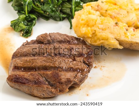 Closeup of seared tenderloin of steak in its juices (au jus) served with stuffed and twice baked potato and wilted spinach.