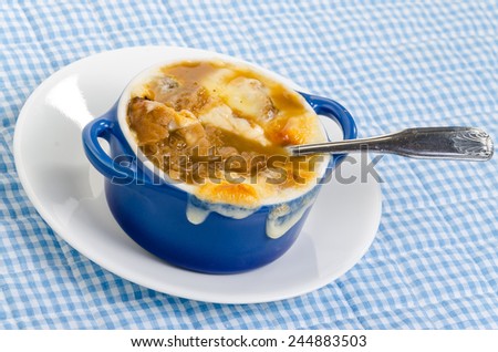 Blue bowl on blue gingham tablecloth with onion juice and melted cheese from French Onion Soup running over the side.