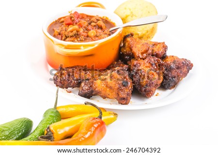 Serving of spicy wings in Honey BBQ Sauce on plate with bowl of homemade chili and Jalapeno cornbread..  Chili Peppers on white background with copy space.