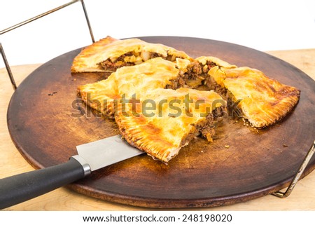 Large family-sized empenada on hot baking stone being sliced into serving size pieces.