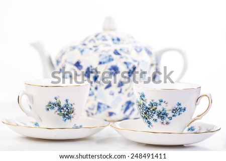 Selective focus on Elegant Fine China Tea Cups in blue floral pattern with tea pot  out of focus in background.