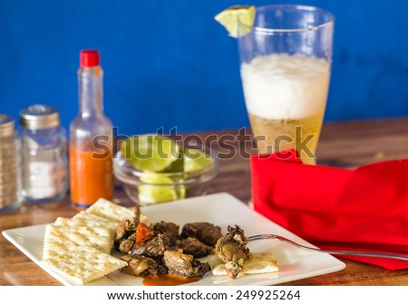 Selective focus on smoked oyster packed with chopped red peppers on saltine crackers and hot sauce.  Served with glass of beer as Happy Hour Snack.