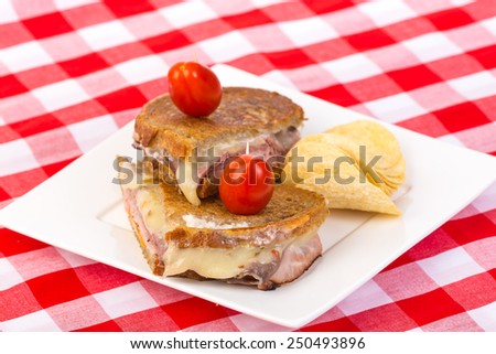 Ham and cheese with roast beef on buttered rye bread grilled under a press and served with chips. Shallow depth of field. Red Plaid Tablecloth.