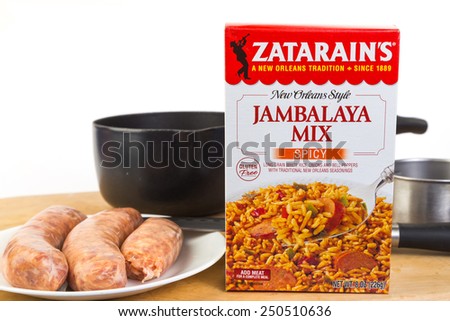 LLANO, TEXAS-FEB 06, 2015: Jambalaya Meal by Zatarain\'s needs only water and choice of meat - sausage in this case.  Cooking utensils on wooden cutting board against white background with copy space.