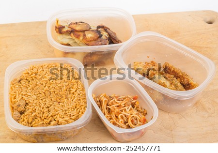 Four plastic containers filled with leftovers - Jambalaya, spaghetti, chicken tenders and onion and potato frittata on wooden cutting board.
