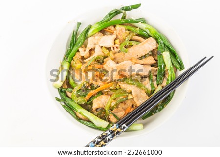 Strong light from upper left on Bowl of pork stir fry over bed of rice in white bowl against white background.  Fancy black chopsticks.
