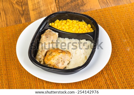 Chicken leg and thigh in plastic microwave dish with mashed potatoes and whole-grain corn.  Typical bland appearance of TV Dinner.